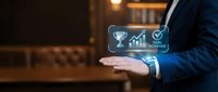 Professional businessman in dark suit presenting digital achievement icons including trophy, growth chart and checkmark in modern office environment.
