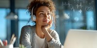 Young woman with curly hair wearing headphones smiles while working on laptop with digital health graphics overlay, perfect for telehealth or medical technology concepts.