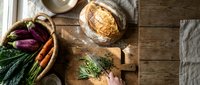 Fresh organic vegetables and artisan bread on rustic wooden table with natural lighting for healthy cooking and farm-to-table dining concepts.