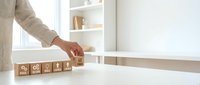 Business professional arranging wooden blocks with percentage symbols on white desk in modern office environment for financial planning concepts.