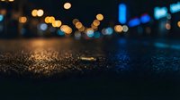 Wet asphalt street surface with bokeh city lights creating atmospheric urban night scene for backgrounds and mood lighting concepts.