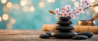 Zen spa composition with stacked black stones, cherry blossom branch and bamboo on wooden surface with soft bokeh lights creating peaceful atmosphere.
