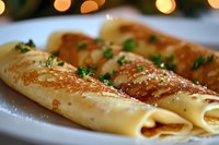 Delicate crepes filled and rolled on white plate garnished with fresh herbs and golden brown crispy edges against soft bokeh lights background.