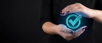 Professional hands protecting glowing checkmark symbol representing quality assurance, verification, approval and business success in corporate environment.