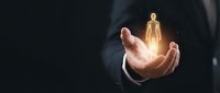 Businessman's hand holding glowing golden human figure against dark background, representing leadership, mentorship, talent management, recruitment, and business success concepts.