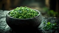 Fresh green pesto sauce in rustic stone bowl on dark background, traditional Italian cuisine preparation with basil, garlic and olive oil.