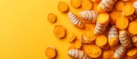 Fresh turmeric and ginger roots scattered on vibrant yellow background, sliced and whole pieces creating organic pattern for healthy cooking and wellness.
