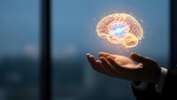 Businessman hands holding glowing brain hologram with neural connections representing artificial intelligence and innovation in modern office.