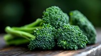 Fresh raw broccoli florets and stems on dark wooden surface, macro view with selective focus showing detailed texture of green vegetable heads.
