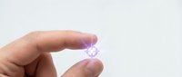 Hand holding small transparent purple crystal or gemstone between fingers on white background for jewelry design and crafting projects.