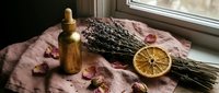 Aromatherapy spa setup with lavender bundle, essential oil bottle and dried orange slice on linen fabric near window for natural wellness and relaxation.