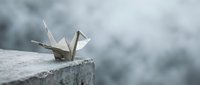 Paper crane origami bird sitting on concrete ledge with soft blurred background symbolizing peace hope and mindfulness meditation concepts.