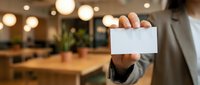 Professional businessman holding blank white business card in modern office space with warm lighting and wooden furniture for corporate branding mockup.