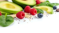 Fresh healthy superfood ingredients with avocado, berries, spinach and chia seeds on white background for clean eating and nutrition concepts.