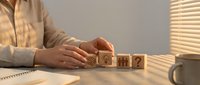 Business professional arranging wooden blocks with question marks and icons on desk, representing problem-solving and decision-making process.