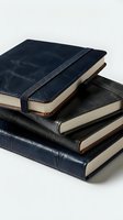 Stack of navy blue and black leather-bound notebooks with elastic closure on white background, evoking elegance and productivity.