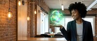 Young African American businesswoman in modern office holding glowing green holographic sphere representing sustainable technology and innovation.