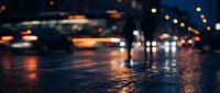 Wet asphalt street at night with blurred car headlights and taillights creating bokeh effect. Urban nighttime scene with reflective pavement and traffic motion blur.