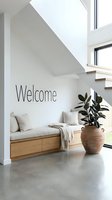 Modern minimalist entryway with wooden bench, linen cushions, terracotta pot, green plant, and Welcome wall text in bright Scandinavian home interior.