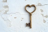 Vintage brass key with heart-shaped handle on weathered white peeling paint wall background for romantic decor projects and love concepts.
