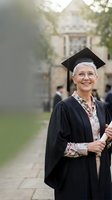 Mature Caucasian woman graduate in cap and gown smiling proudly on university campus after commencement ceremony celebrating academic achievement and lifelong learning.