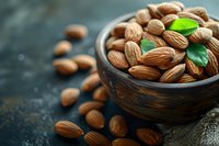 Fresh whole almonds in rustic wooden bowl with green leaves on dark textured background, selective focus with copy space for healthy eating concept.