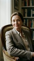 Professional mature Caucasian businesswoman in gray suit sitting confidently in vintage armchair at home office with bookshelf background for corporate portraits.