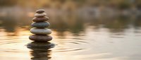 Zen stone stack balanced on calm water surface creating ripples at sunset. Meditation and mindfulness concept for wellness, spa treatments, and spiritual balance practices.