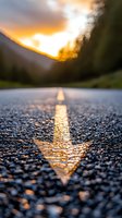Dramatic sunset reflection on wet asphalt road with yellow line marking. Close-up ground level view captures golden hour light and mountain silhouette in background.