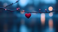 Red heart pendant hanging on bare tree branch against blurred blue bokeh background, romantic Valentine's day composition with soft evening light and dreamy atmosphere.