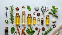 Natural essential oils in glass bottles with fresh herbs and spices arranged on white background for aromatherapy and wellness applications.