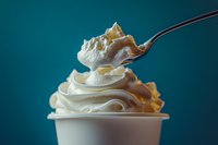 Spoon lifting creamy soft serve ice cream with caramel swirl from white cup against teal background, dessert and indulgence concept for food advertising.