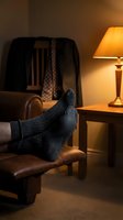 Cozy evening relaxation scene with feet in warm wool socks resting on leather armchair beside glowing table lamp in comfortable living room interior.
