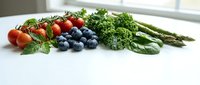 Fresh organic vegetables and berries on white kitchen counter including cherry tomatoes, blueberries, kale and asparagus for healthy cooking and nutrition.