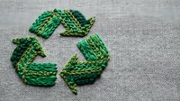 Green embroidered recycling symbol on gray fabric background representing sustainability and environmental awareness for eco-friendly projects.