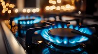 Blue gas flame burning on modern kitchen stove with golden bokeh lights in background, close-up view showing energy consumption and cooking concept.