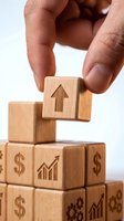 Hand placing wooden block with upward arrow on pyramid of business symbol cubes representing growth strategy and financial success building concepts.