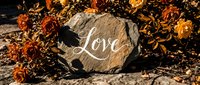 Stone with handwritten Love inscription surrounded by autumn dried flowers in warm orange tones, romantic fall garden decor concept.
