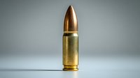 Single brass bullet with copper tip standing upright on reflective surface against gray background, dramatic studio lighting highlights metallic texture.