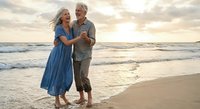 Happy mature couple dancing on beach at sunset, romantic vacation lifestyle, elderly man and woman enjoying retirement together on ocean shore.