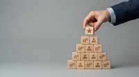 Businessman hand placing wooden block with star icon on top of pyramid structure representing business growth, success, and organizational hierarchy for corporate strategy and leadership concepts.