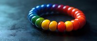 Colorful rainbow beaded bracelet on dark textured background with vibrant gradient from blue to red, showcasing pride colors in circular jewelry design.
