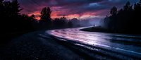 Dramatic twilight landscape with glowing river reflecting vibrant purple and pink sky, silhouetted trees lining banks, moody atmospheric scene for nature and travel projects.
