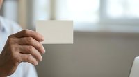 Man with dark skin tone holding blank white card in office setting, suitable for business messaging and corporate communications.