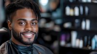 Smiling African American man with dreadlocks in professional salon setting with hair care products on shelves in background for barbershop services.