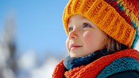 Young Caucasian girl in colorful knitted winter hat and scarf looking up with wonder against blue sky background. Winter childhood joy and outdoor activities concept.