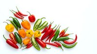 Assorted fresh chili peppers and bell peppers arranged on white background, including red, green, yellow and orange varieties for cooking and culinary design projects.