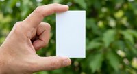 Hand holding blank white business card mockup against green nature background for branding and marketing design projects.