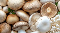 Fresh white button mushrooms and portobello caps arranged with gills visible, showing texture and natural patterns in warm earth tones, suitable for food photography.