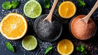 Fresh citrus slices with black and pink Himalayan salt in wooden spoons on dark background, garnished with mint leaves and scattered salt crystals.